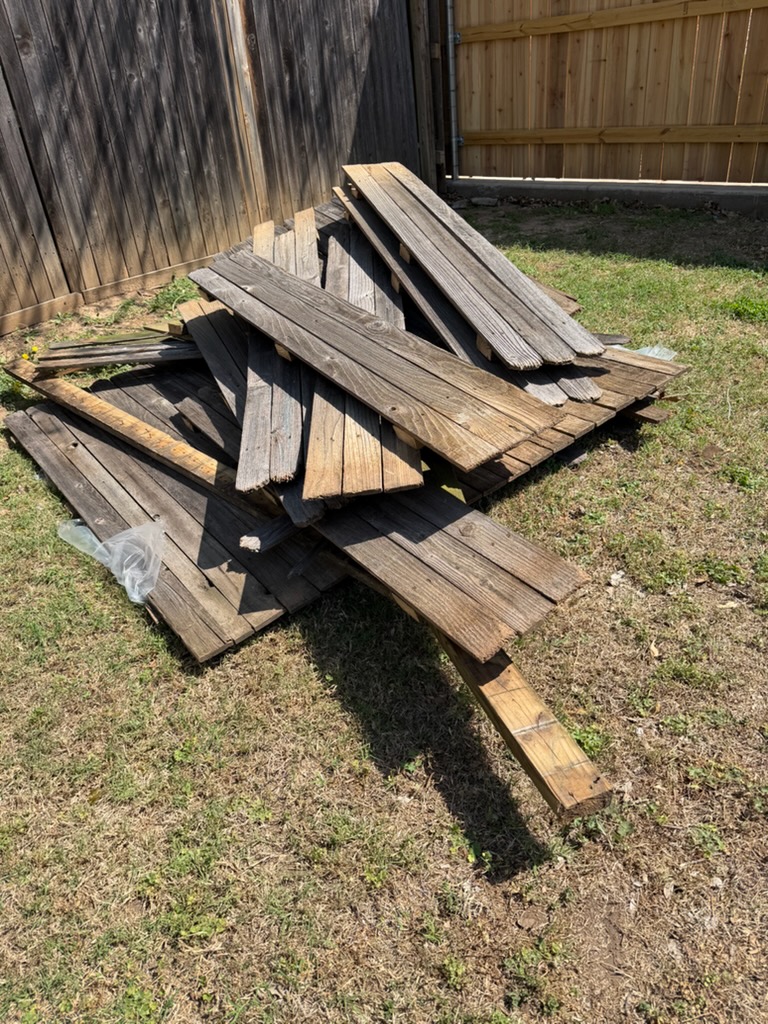 Pile of wood boards awaiting removal beside a backyard fence