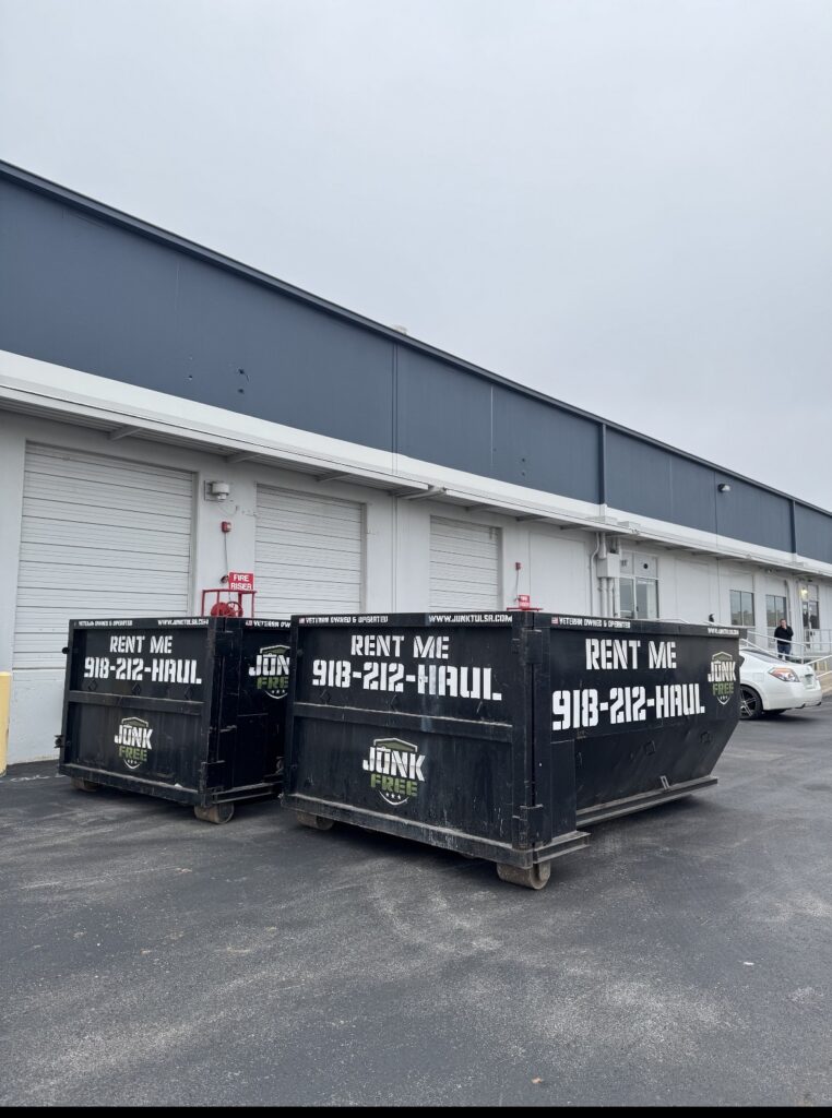 Two Junk Free 15-yard roll-off dumpsters beside warehouse loading doors