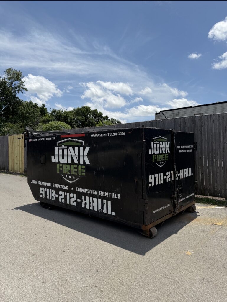 Black Junk Free 20-yard dumpster with shield branding beside a fence