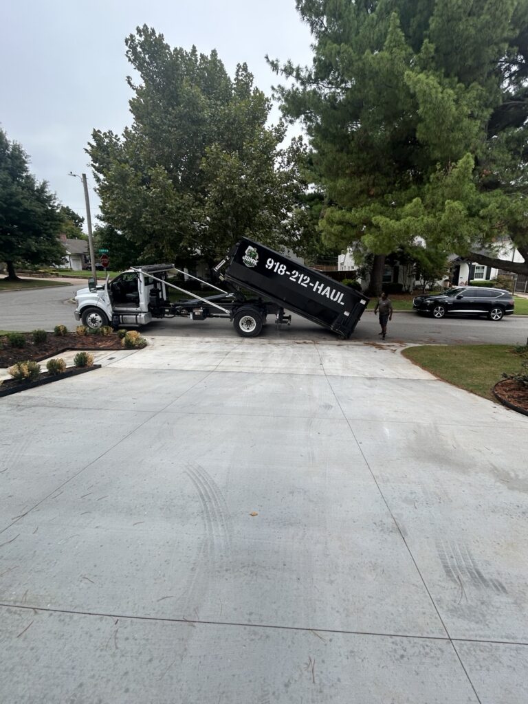 Junk Free truck lowering a black roll-off dumpster at a residential driveway