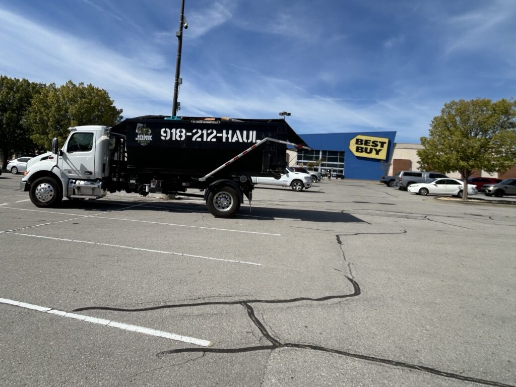 Junk Free roll-off truck carrying a black dumpster in a shopping center parking lot