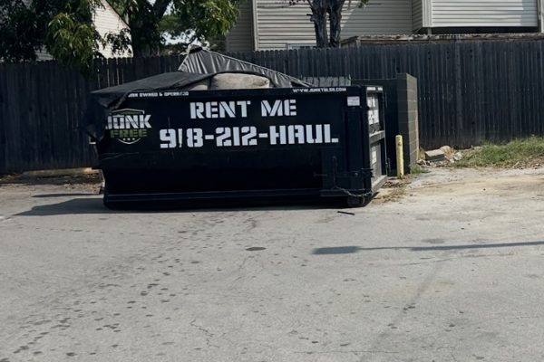Black Junk Free rental dumpster beside a fence near a residential building