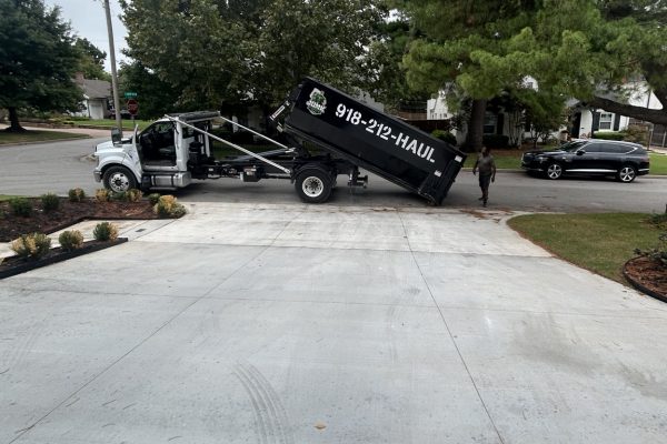 Junk Free truck lowering a black roll-off dumpster at a residential driveway