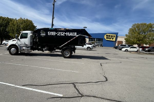Junk Free roll-off truck carrying a black dumpster in a shopping center parking lot